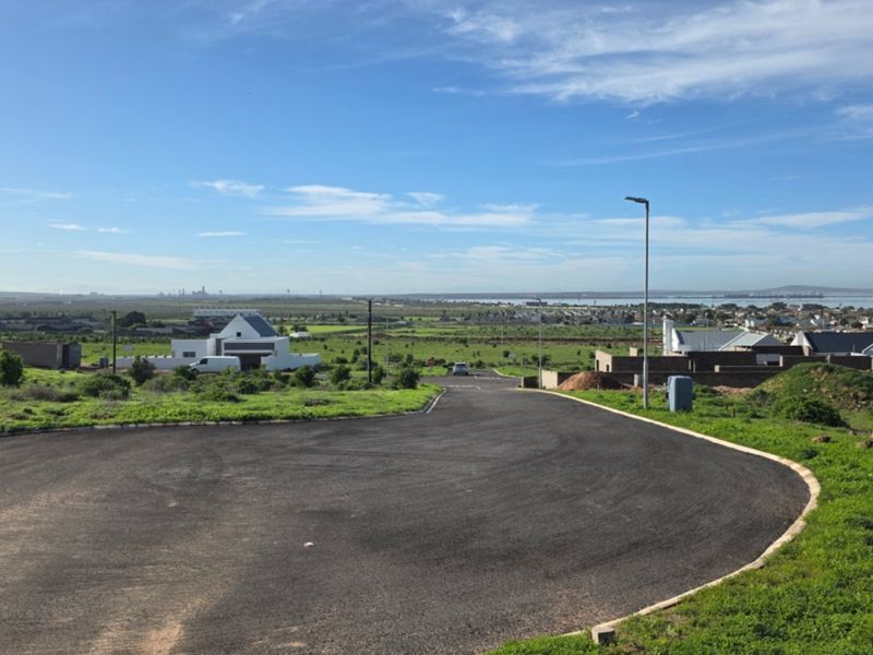 A wide-angle view of a residential development area featuring paved roads, street lighting, and surrounding landscape with distant coastal views.
