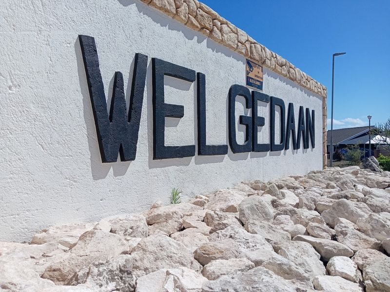 A view of the Welgedaan estate entrance wall featuring stone cladding, signage, and decorative rock landscaping.