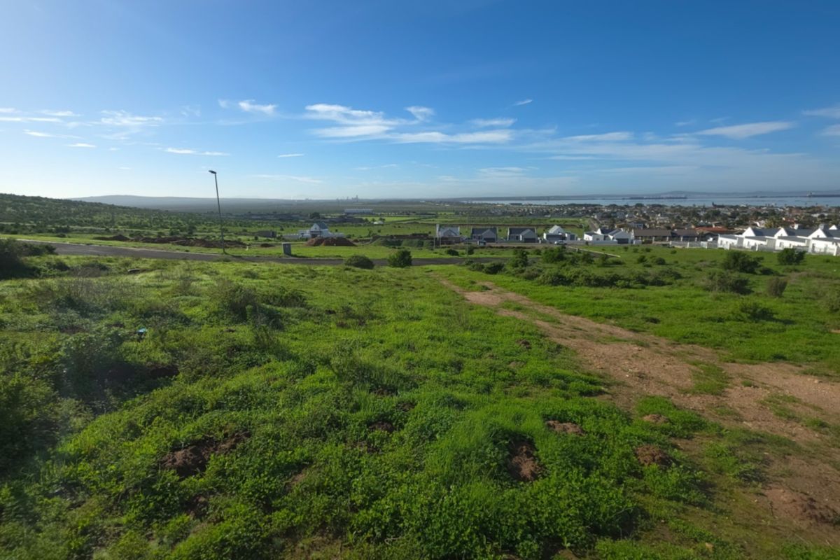 A wide-angle view of the vacant residential land, showcasing the surrounding landscape, nearby neighborhood, and distant coastal horizon.
