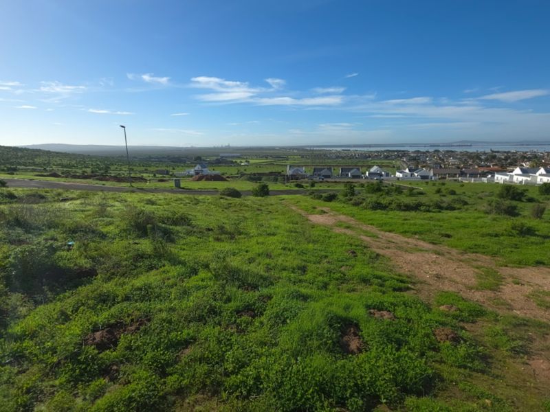 A wide-angle view of the vacant residential land, showcasing the surrounding landscape, nearby neighborhood, and distant coastal horizon.