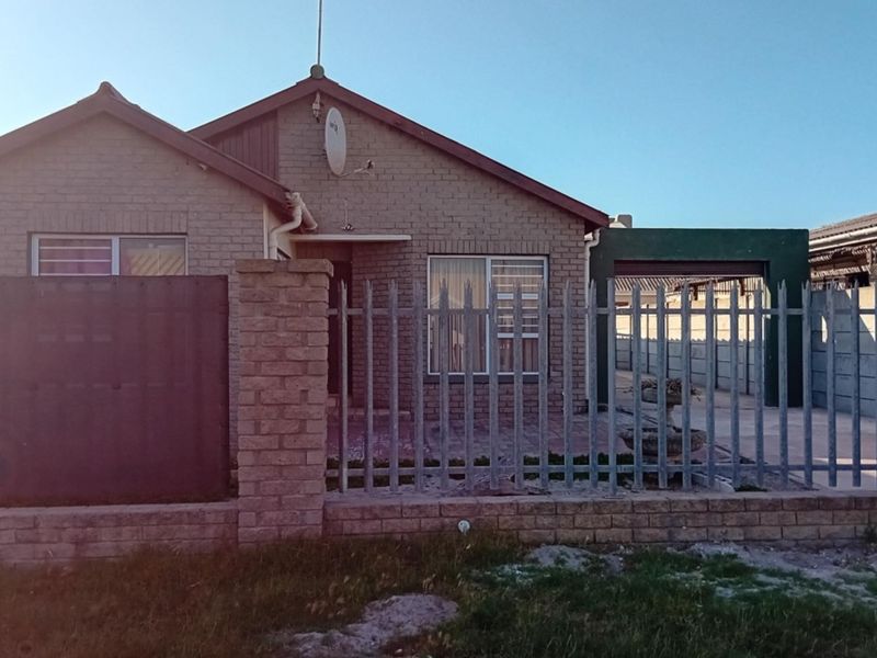 Front view of a single-story facebrick house featuring a secure metal fence, brick boundary wall, and a covered carport area.