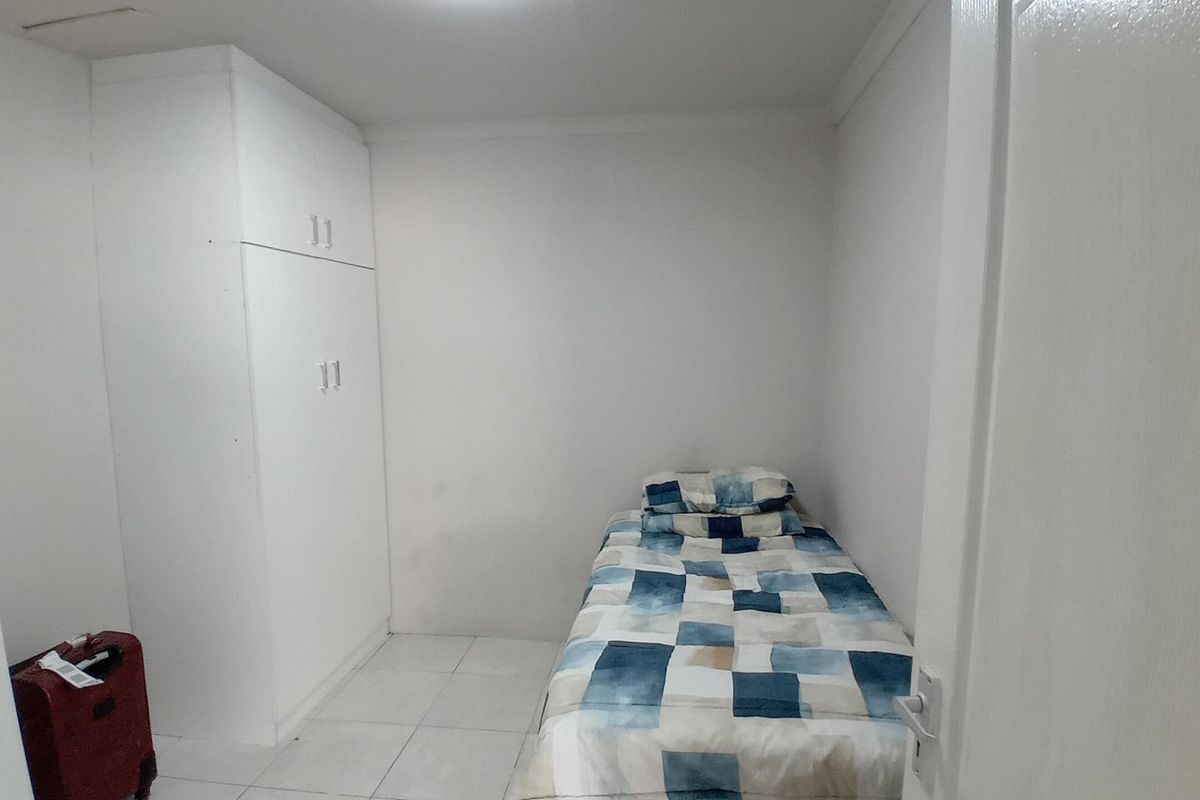 A compact bedroom featuring white walls, tiled flooring, and a built-in wardrobe for storage.