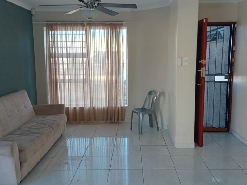 A living room featuring tiled flooring, a ceiling fan, and security features on the window and entrance door.