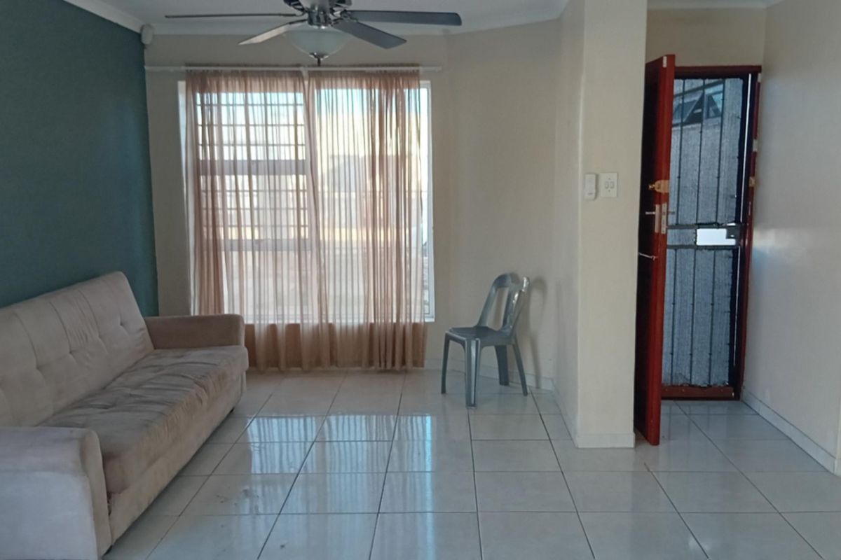 A living room featuring tiled flooring, a ceiling fan, and security features on the window and entrance door.