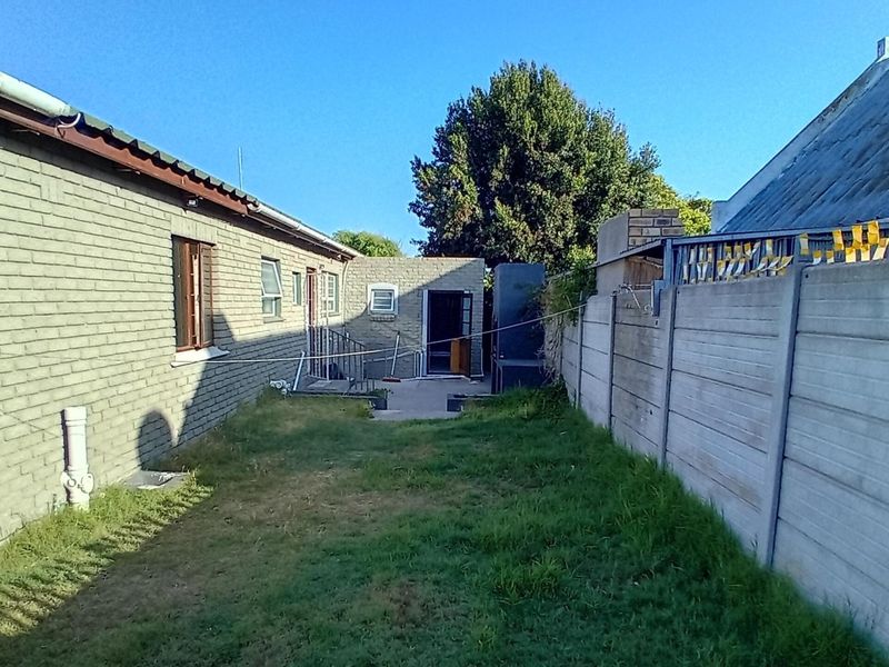 A view of the rear exterior of the property featuring a brick facade, a paved walkway, and a precast concrete boundary wall.