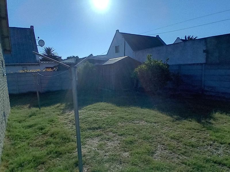 A rear garden area featuring a lawn, a storage shed, and a precast concrete boundary wall.