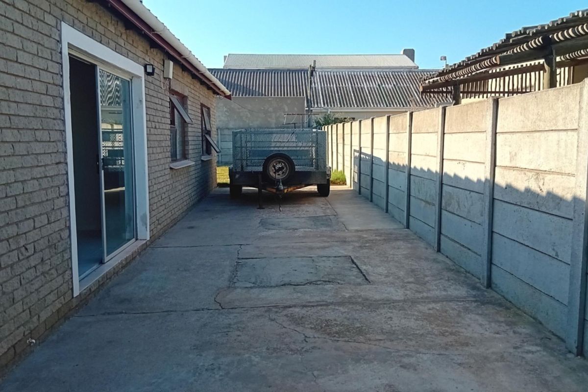 A side exterior view of the property featuring a concrete driveway, brick wall construction, and a precast concrete boundary fence.