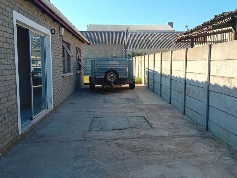 A side exterior view of the property featuring a concrete driveway, brick wall construction, and a precast concrete boundary fence.