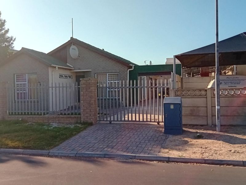 Front view of a single-story brick house featuring a paved driveway, metal security gate, and a carport, enclosed by a precast boundary wall.