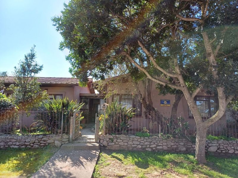 Front elevation of a single-story house featuring a stone retaining wall, metal fencing, and a concrete pathway leading to the entrance.