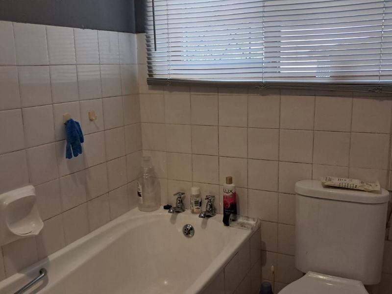 A functional bathroom featuring a standard bathtub, toilet, and tiled wall finishes, requiring cosmetic updates to improve its overall aesthetic appeal.