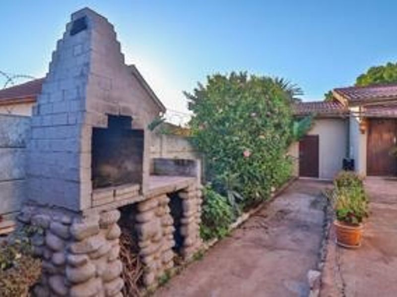 Rear exterior area featuring a built-in brick braai, paved patio space, and perimeter wall with security fencing.