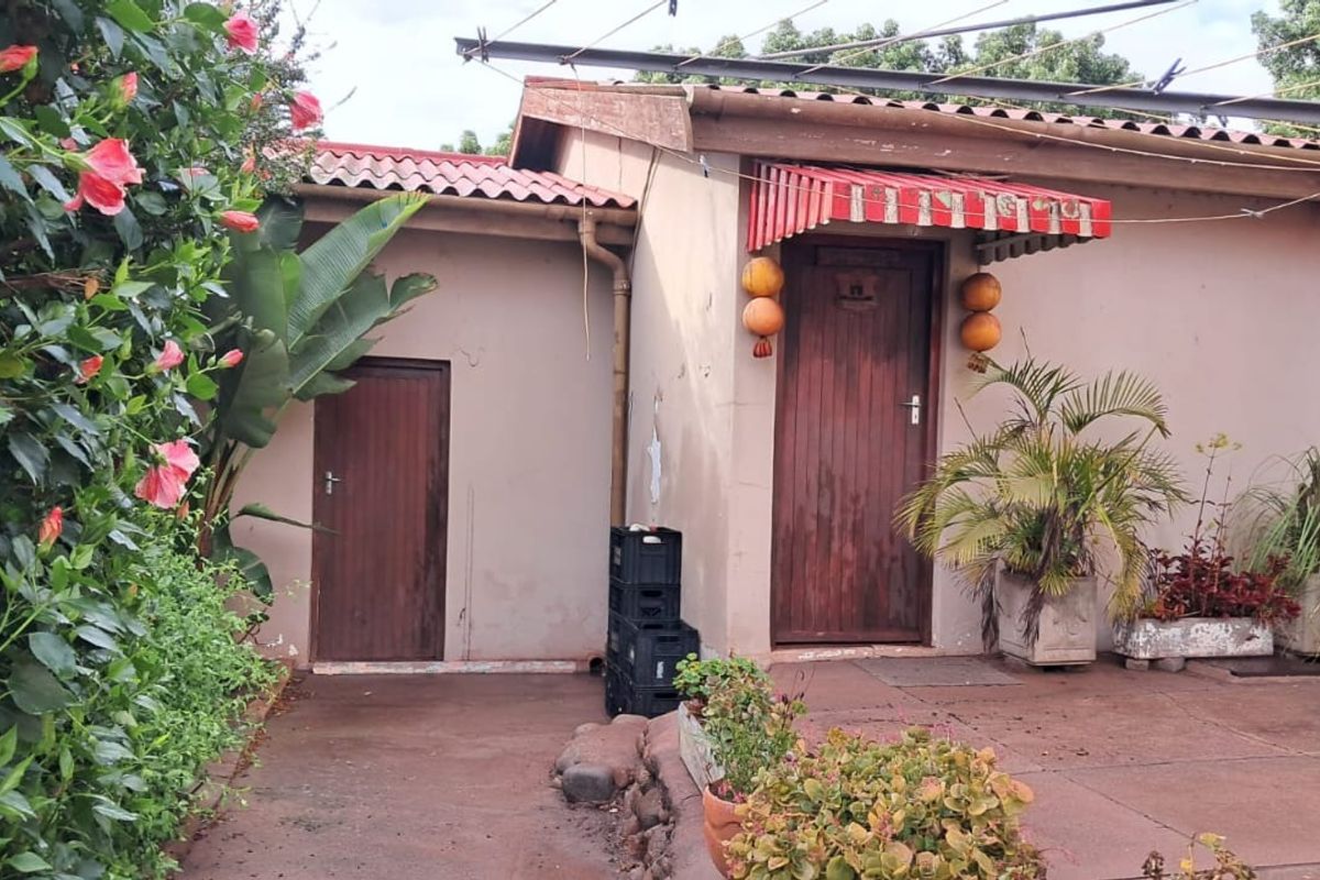 Rear exterior view of the property featuring a paved patio area, tiled roof, and two wooden entrance doors with a striped awning.