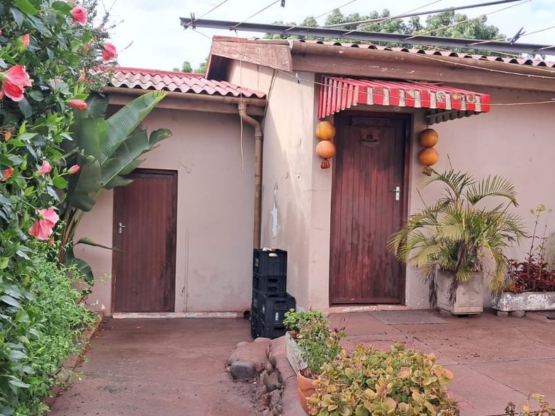 Rear exterior view of the property featuring a paved patio area, tiled roof, and two wooden entrance doors with a striped awning.