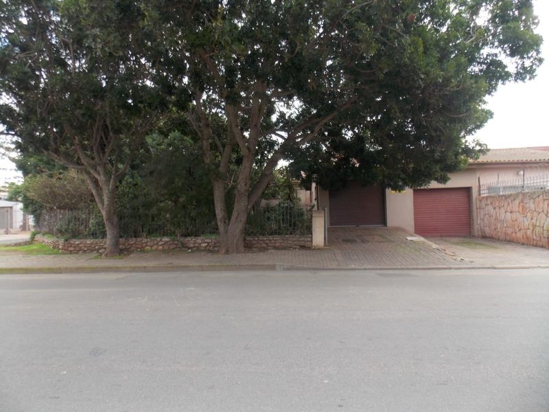 Front view of the property featuring a double garage, paved driveway, and established trees behind a stone and metal boundary wall.