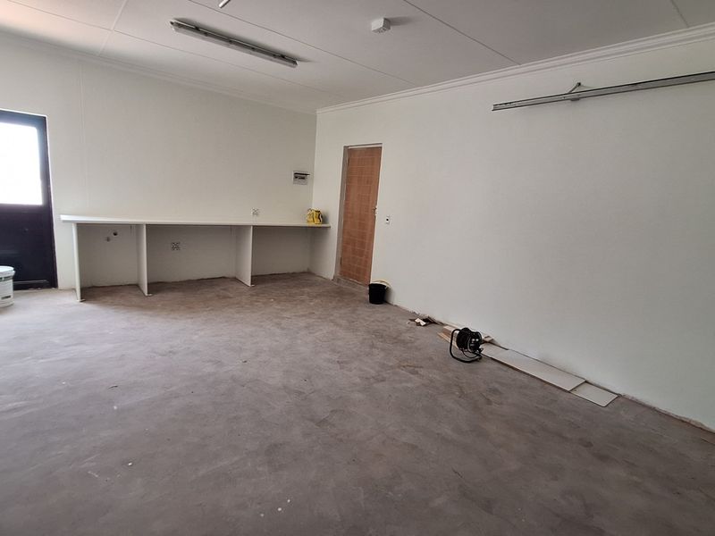 An unfinished utility space featuring a built-in workbench, concrete flooring, and direct external access, suitable for a workshop or storage area.