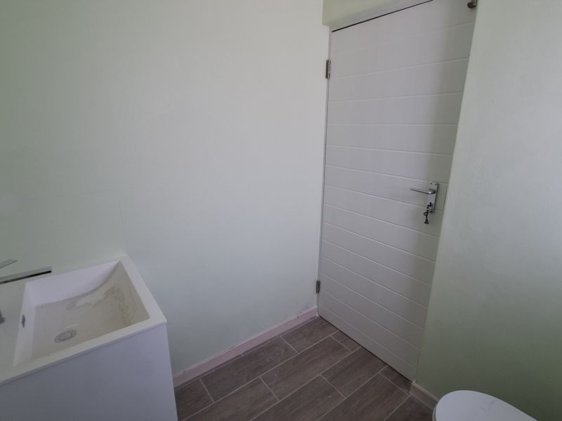 A clean, minimalist bathroom featuring a modern vanity basin with a mixer tap and neutral tiled flooring.