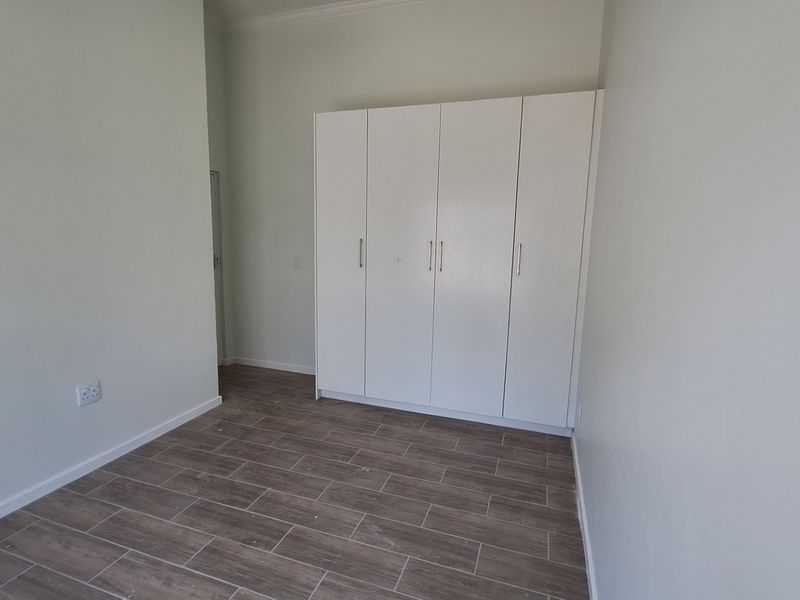 A clean, empty bedroom featuring modern wood-look tiled flooring and ample built-in cupboard storage space.