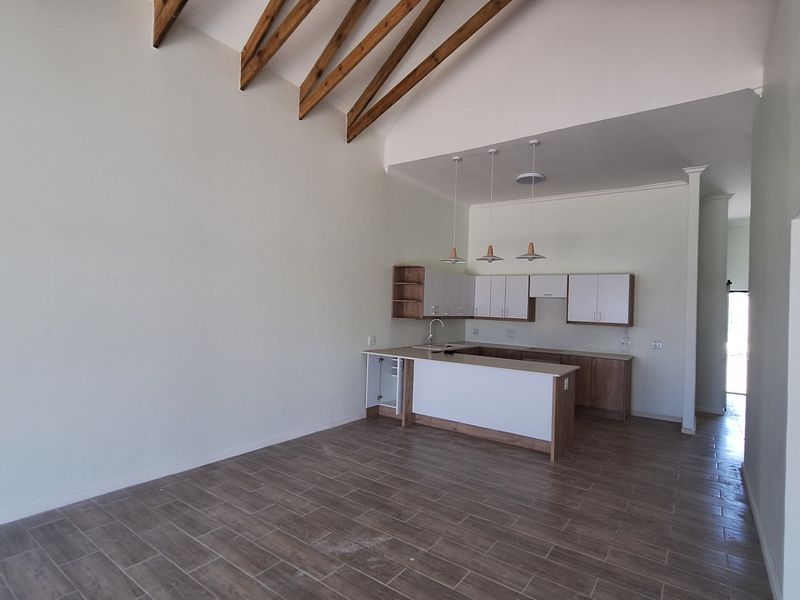 Spacious open-plan living and kitchen area featuring high vaulted ceilings with exposed timber trusses and modern tiled flooring.