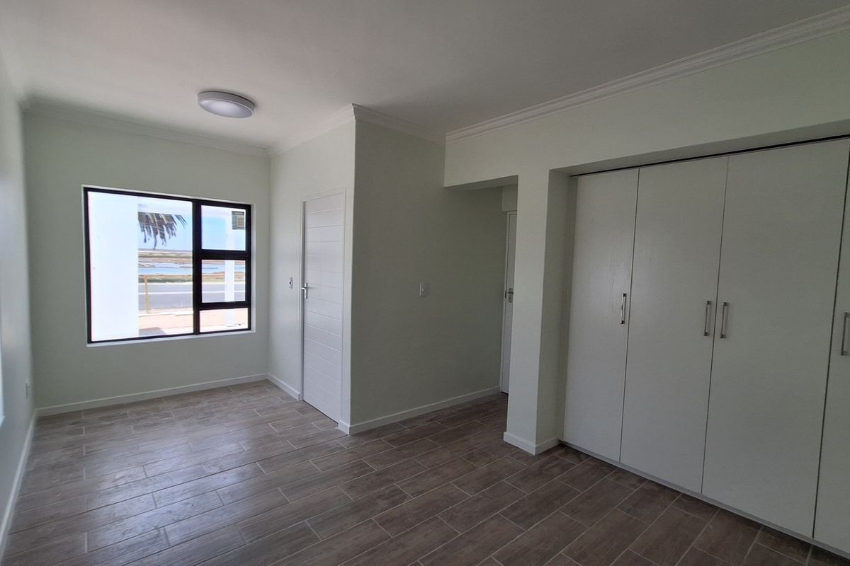 A bright, empty bedroom featuring modern tiled flooring, built-in cupboards, and a window with a view.