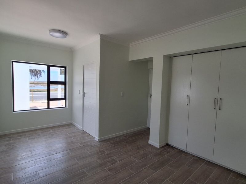 A bright, empty bedroom featuring modern tiled flooring, built-in cupboards, and a window with a view.