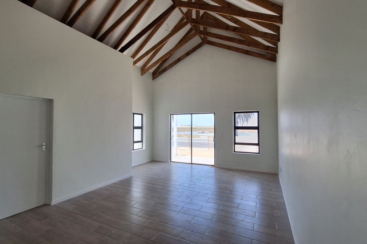 Spacious living area featuring a high vaulted ceiling with exposed timber trusses, tiled flooring, and large windows providing natural light and exterior views.