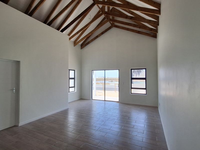 Spacious living area featuring a high vaulted ceiling with exposed timber trusses, tiled flooring, and large windows providing natural light and exterior views.