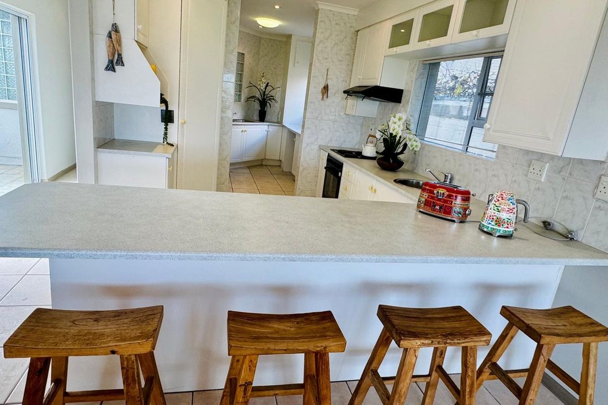 A functional kitchen featuring white cabinetry, laminate countertops, a breakfast bar, and a separate scullery area with tiled finishes throughout.