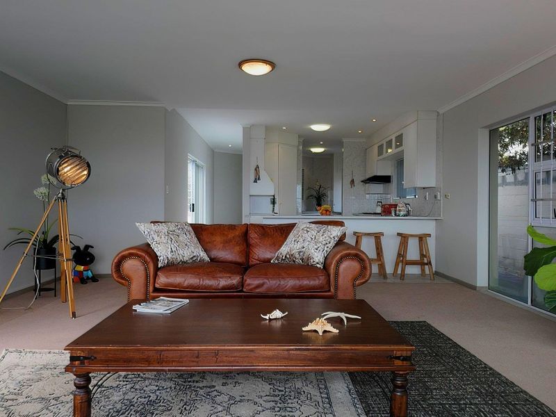 Open plan living area featuring a kitchen with white cabinetry and a breakfast bar, flowing into a spacious lounge with sliding door access.
