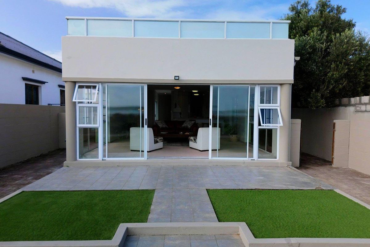 Rear view of the property featuring a tiled patio, artificial lawn, and large sliding glass doors leading into the living area.