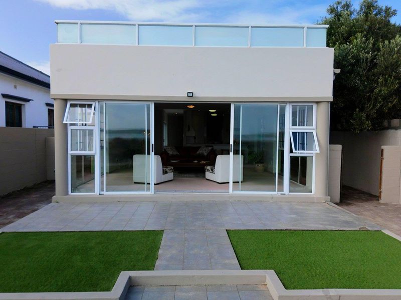 Rear view of the property featuring a tiled patio, artificial lawn, and large sliding glass doors leading into the living area.