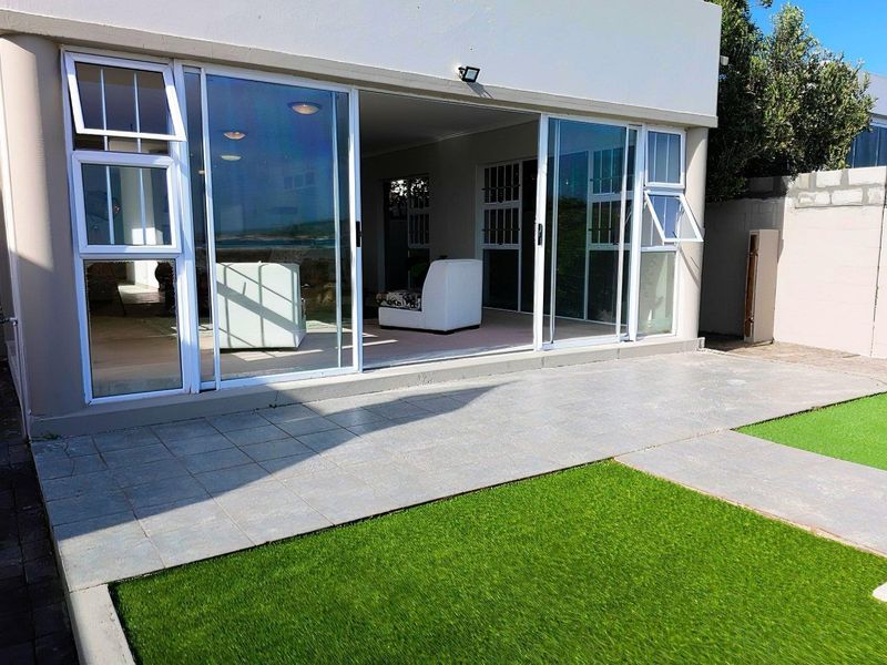 Rear view of the property featuring a tiled patio area, artificial lawn, and large sliding glass doors providing access to the interior living space.
