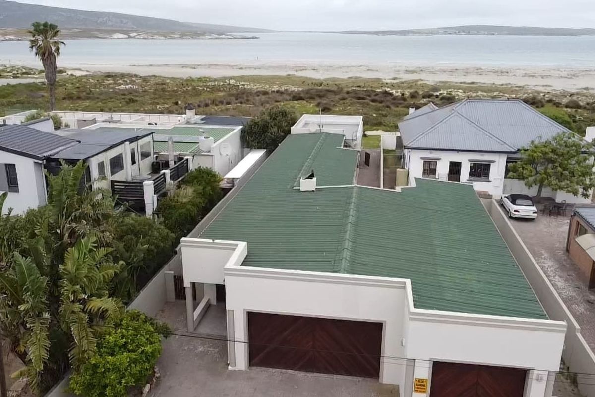 Aerial view of the property featuring a green corrugated metal roof, double garage, and paved driveway, situated in a coastal location.
