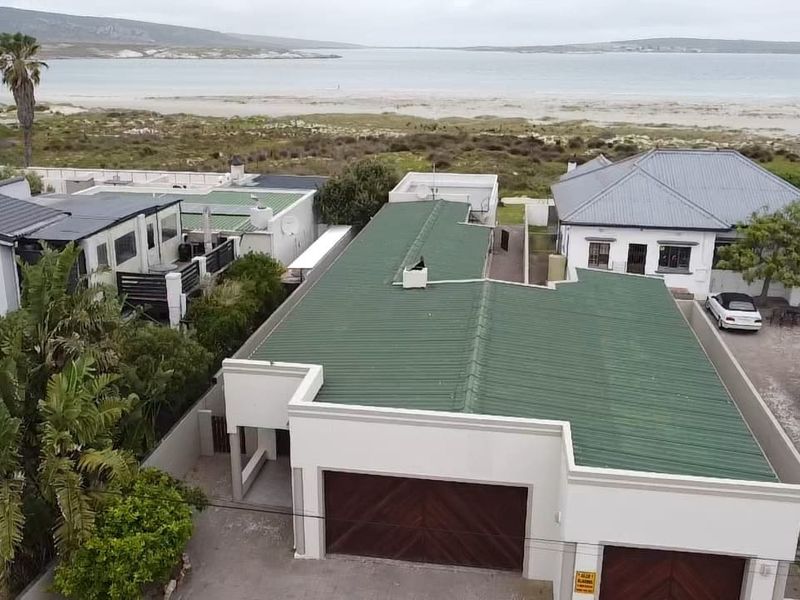 Aerial view of the property featuring a green corrugated metal roof, double garage, and paved driveway, situated in a coastal location.