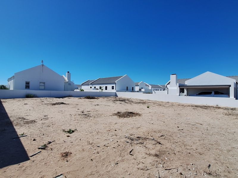 A vacant, sandy plot of land enclosed by a white boundary wall, situated within a residential estate setting.