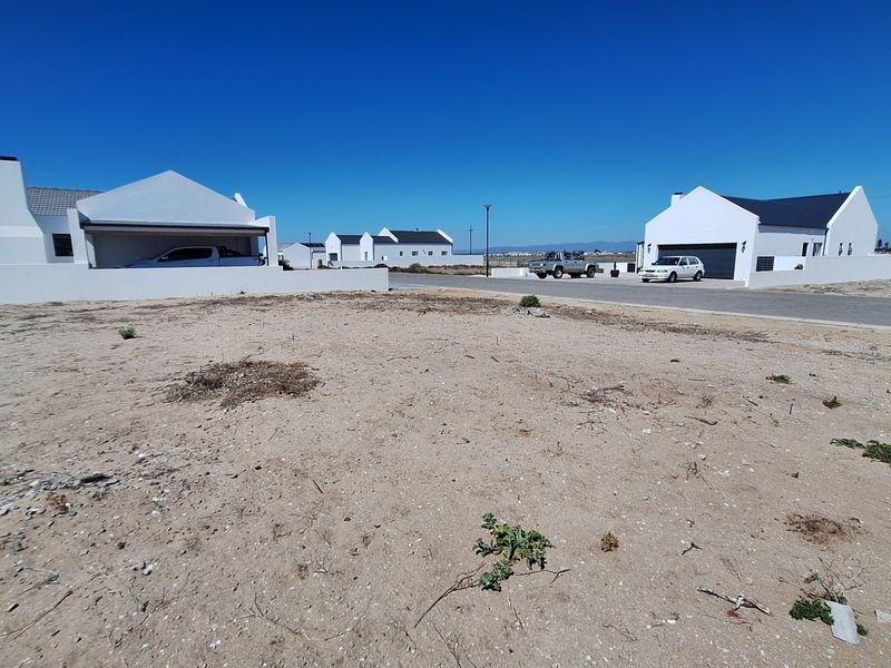 A view of a vacant residential plot situated in a developed neighborhood with paved street access and surrounding modern homes.