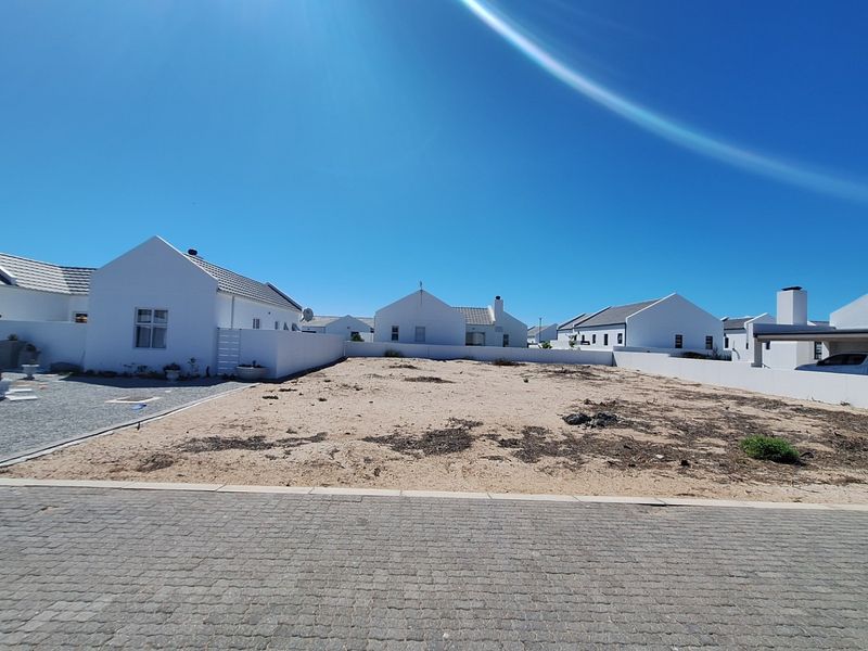 A vacant residential plot featuring a paved driveway, boundary walls, and an adjacent carport structure in a quiet estate setting.