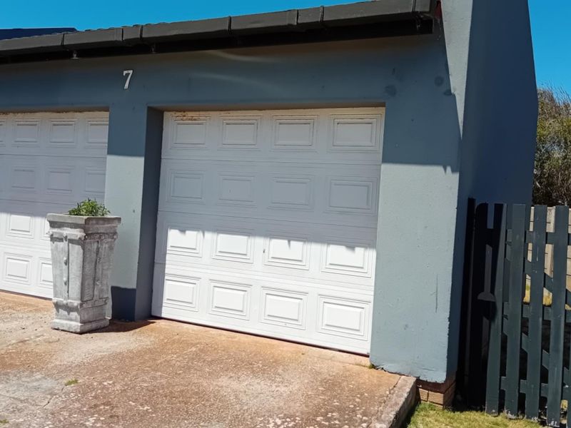 A double garage exterior featuring white sectional doors, a concrete driveway, and a side access gate.