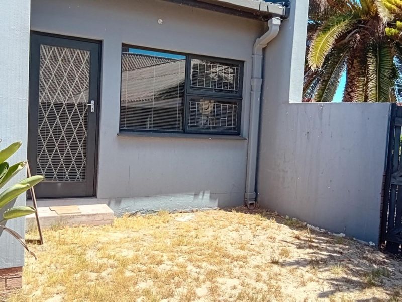 A rear exterior view of the property featuring a security gate, aluminium window, and a small garden area with a timber side gate.