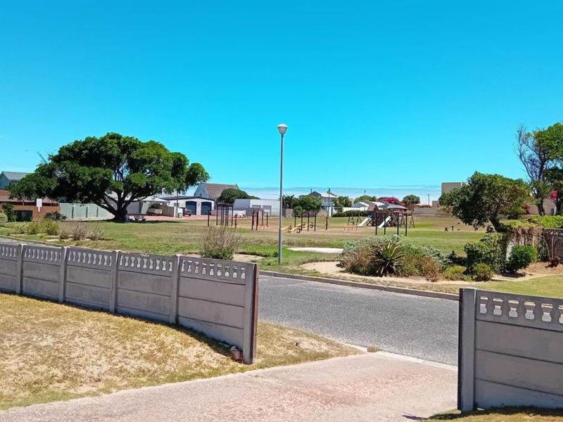 A street-level view showing a residential neighbourhood approach with a precast concrete boundary wall and paved driveway access.