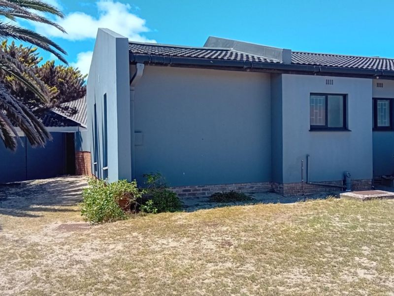 Rear view of the property featuring a grey rendered facade, tiled roof, and aluminium window frames with security bars.