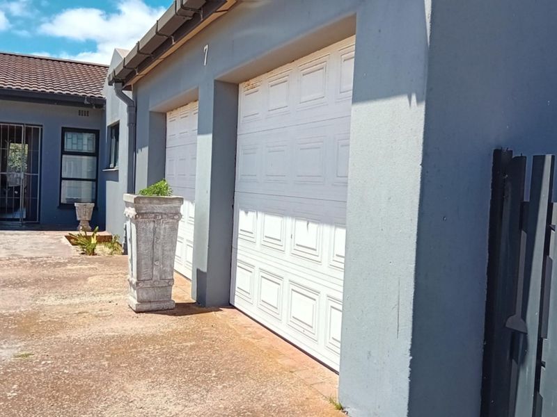 Exterior view of a double garage with white sectional doors and a paved driveway, featuring a secure entrance gate to the side.