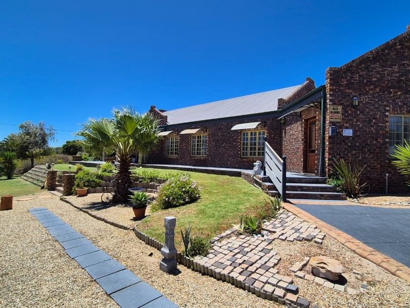 A well-maintained face brick house featuring a metal roof, paved driveway, and landscaped garden with stone retaining walls.