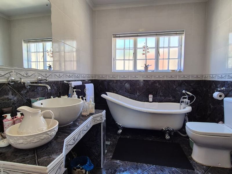 A classic bathroom featuring a clawfoot bathtub, vessel sink with wall-mounted tap, and dark tiled finishes with a large wall mirror.
