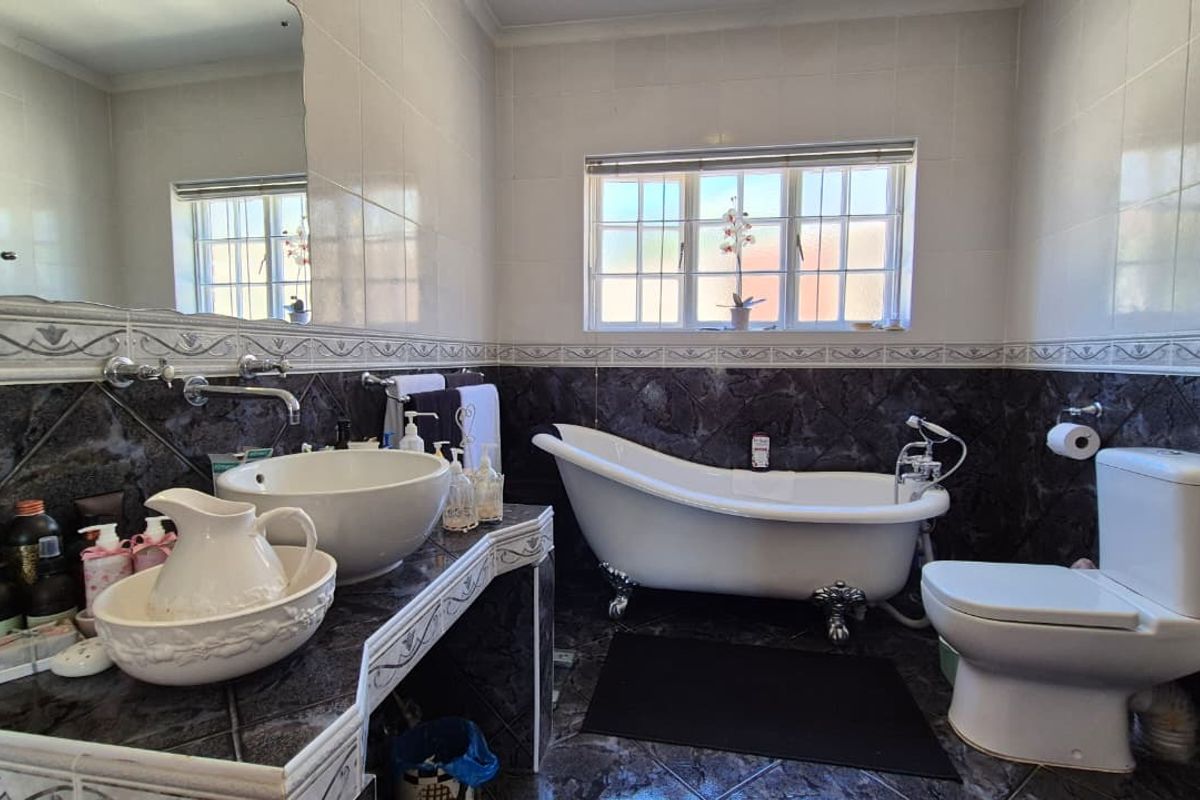 A classic bathroom featuring a clawfoot bathtub, vessel sink with wall-mounted tap, and dark tiled finishes with a large wall mirror.
