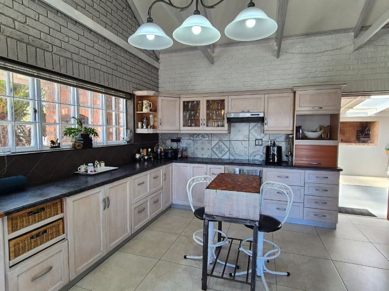 A spacious kitchen featuring light-toned cabinetry, exposed brick walls, vaulted ceilings, and a tiled backsplash, offering a rustic yet functional cooking environment.