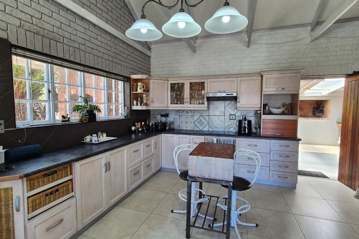 A spacious kitchen featuring light-toned cabinetry, exposed brick walls, vaulted ceilings, and a tiled backsplash, offering a rustic yet functional cooking environment.