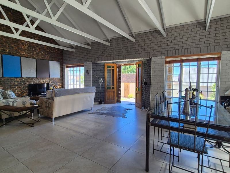 Spacious open-plan living and dining area featuring exposed brick walls, vaulted ceilings with white trusses, and large windows providing natural light.