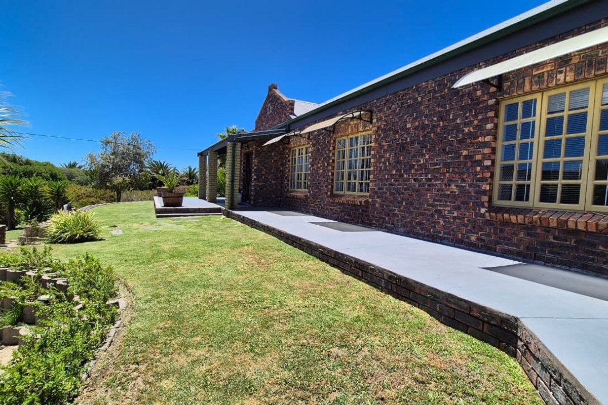 A well-maintained rear exterior view of a face brick house featuring a concrete patio, metal window frames, and established garden surroundings.