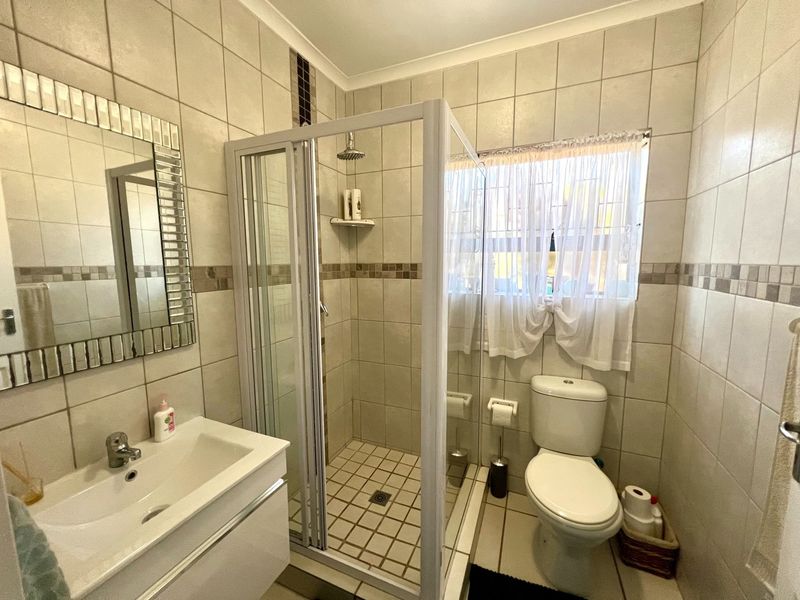 A functional bathroom featuring a glass-enclosed shower, a modern vanity basin, and a toilet, finished with neutral wall and floor tiling.